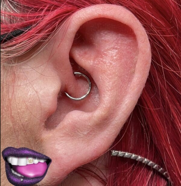 A woman with red hair and purple lips wearing an ear piercing.