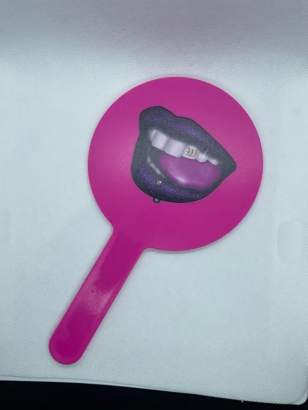 A pink hand mirror with a picture of lips on it.