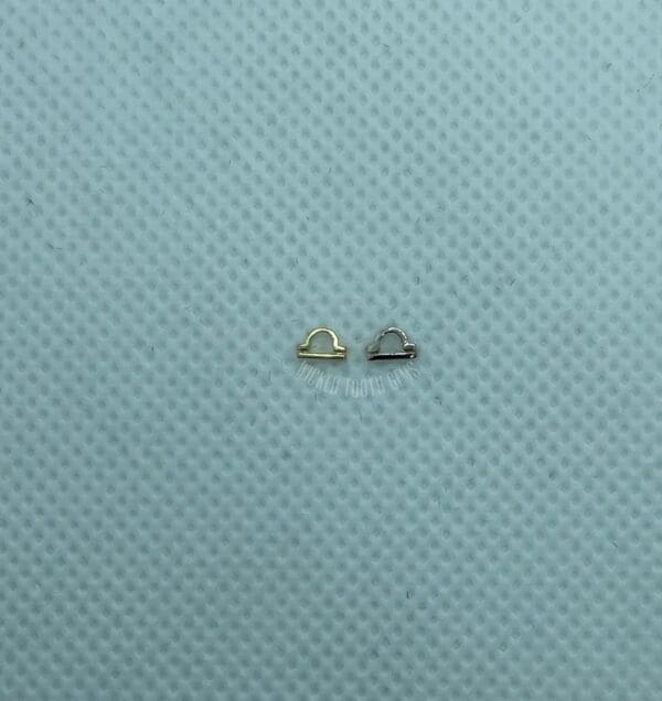 A pair of tiny gold earrings sitting on top of a blue surface.