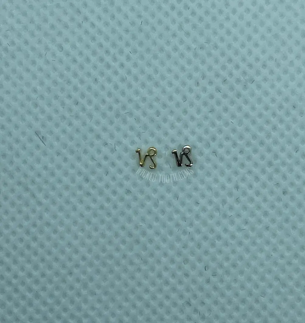 A pair of tiny gold earrings sitting on top of a blue cloth.