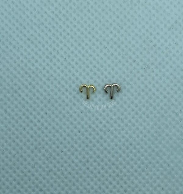 A pair of tiny gold plated earrings sitting on top of a blue background.